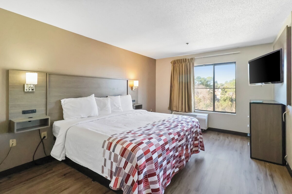 A hotel room with a large bed, a TV, a desk, and a window with curtains.
