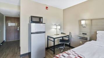 Habitación de hotel con cama, escritorio con silla, refrigerador, microondas, lámpara, teléfono y mesita de noche.