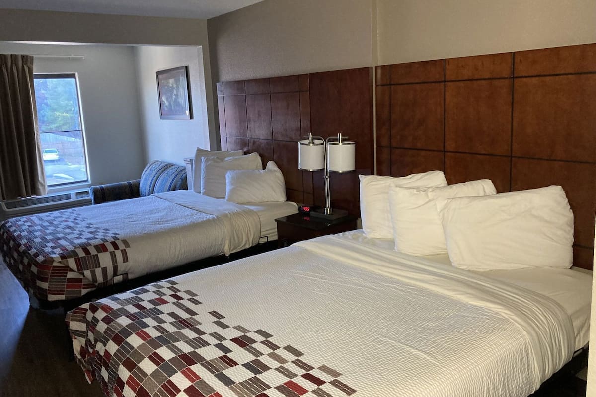 A hotel room with two beds, a window with curtains, a bedside table with lamps, and a wall-mounted picture.