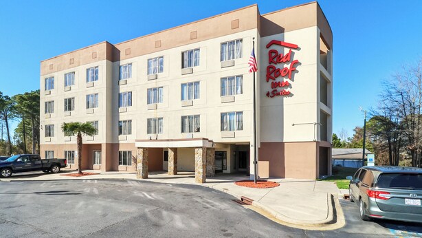 A hotel with a modern design, featuring a prominent red sign, multiple windows, and a parking area with several cars. - Red Roof Inn & Suites Fayetteville - Fort Bragg (Fayetteville)