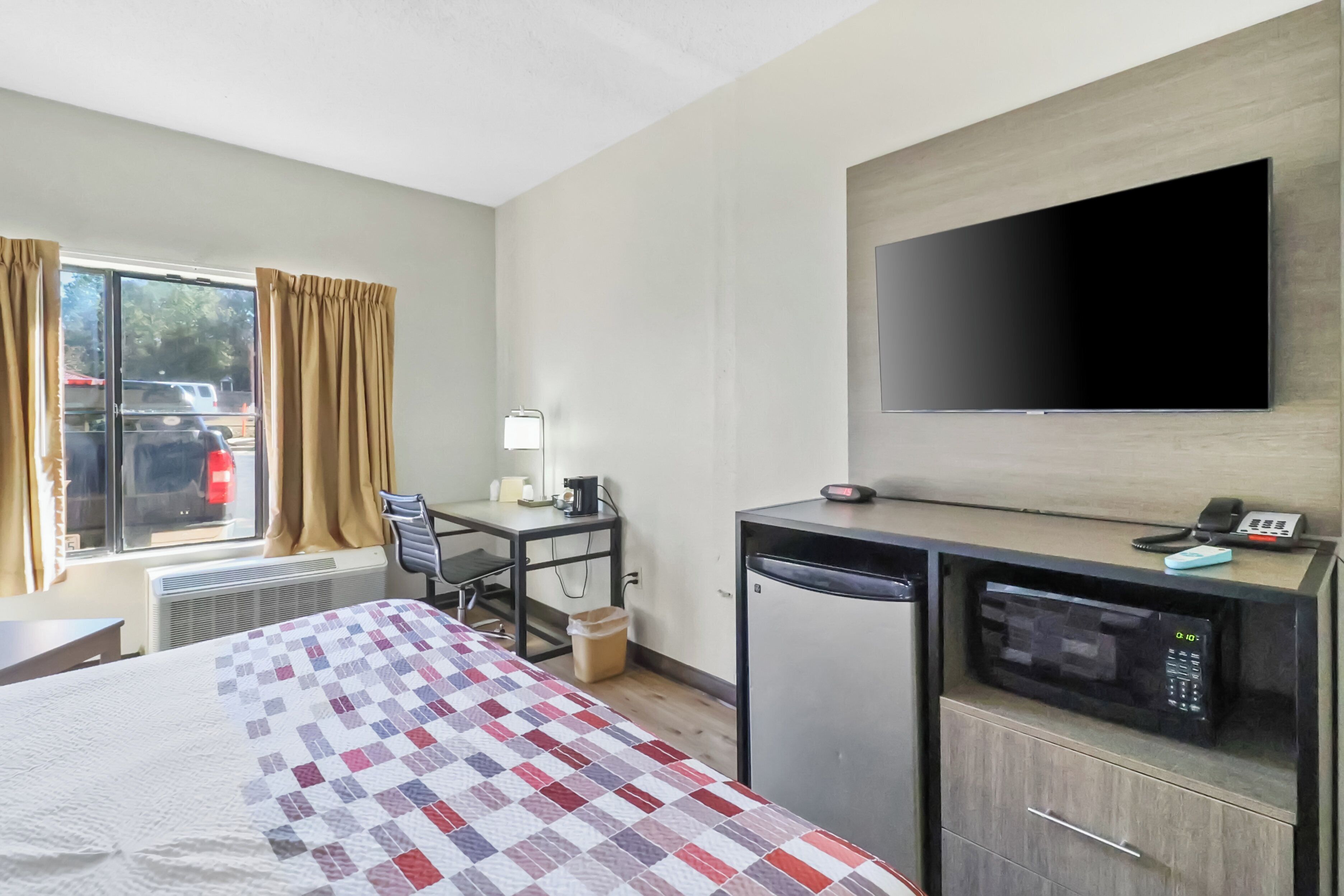 A hotel room with a bed, desk, chair, television, and a microwave.
