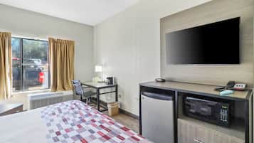 A hotel room with a bed, desk, chair, television, and a microwave.