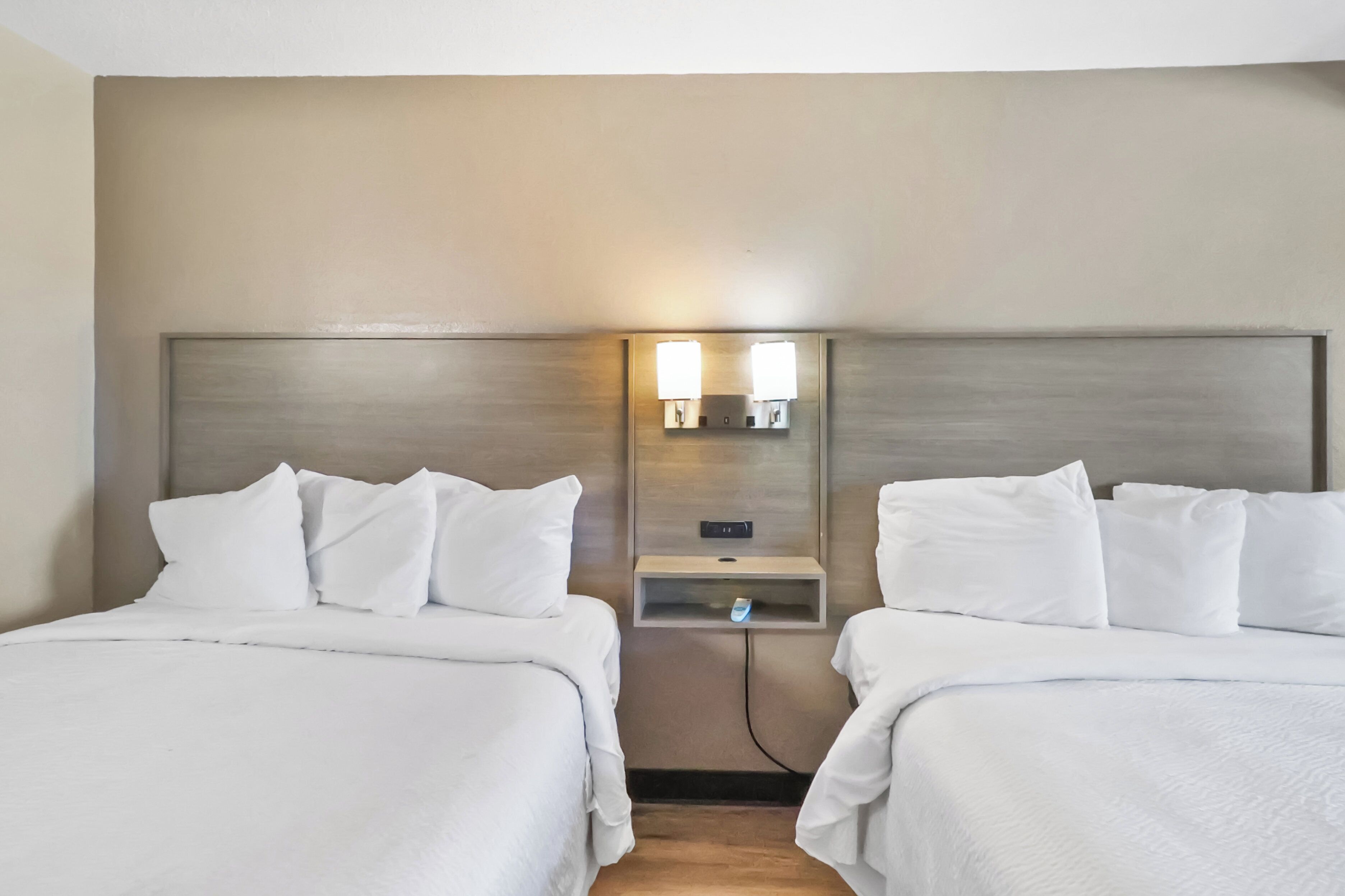 Ein Hotelzimmer mit zwei Betten, jeweils mit weißer Bettwäsche und Kissen. Eine Wandleuchte befindet sich zwischen den Betten.