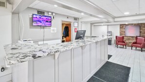 A reception area with a marble counter, a flat-screen TV, a computer, and a seating area with red chairs. - Red Roof Inn & Suites Fayetteville - Fort Bragg (Fayetteville)