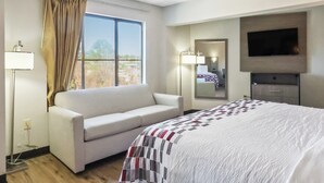 Habitación de hotel con cama, sofá, televisión, ventana con cortinas y lámpara de noche.
