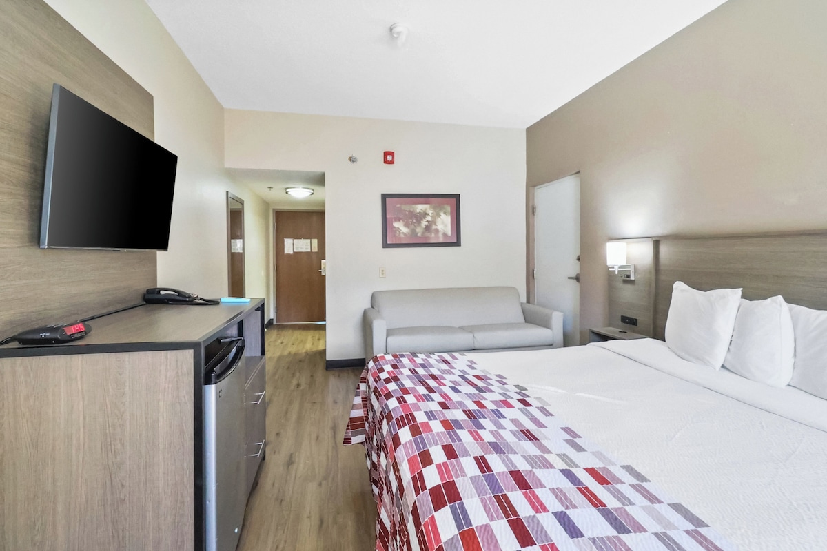 A hotel room with a bed, a desk, a television, a sofa, and a painting on the wall.