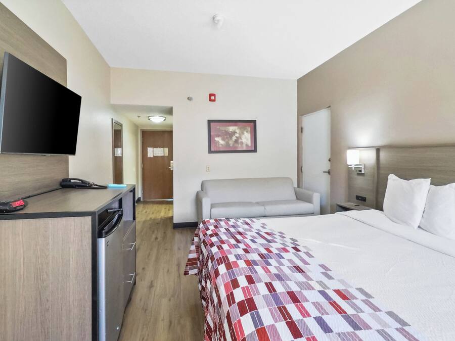 A hotel room with a bed, a desk, a television, a sofa, and a painting on the wall.