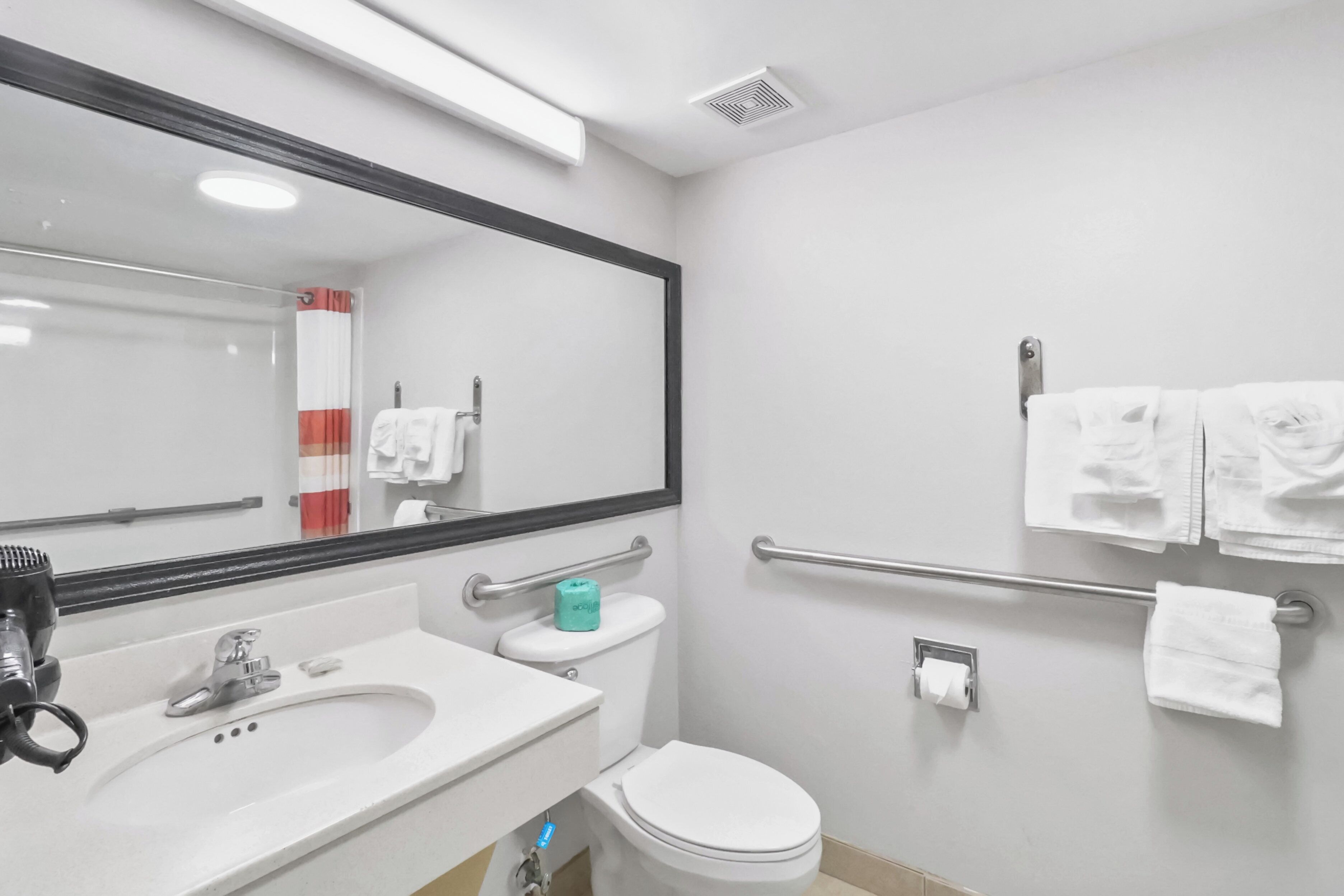 Un baño con lavamanos, espejo, inodoro y toallero.