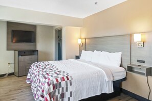 Quarto de hotel com cama, televisão de tela plana na parede, mesa de cabeceira com abajur e armário embutido.