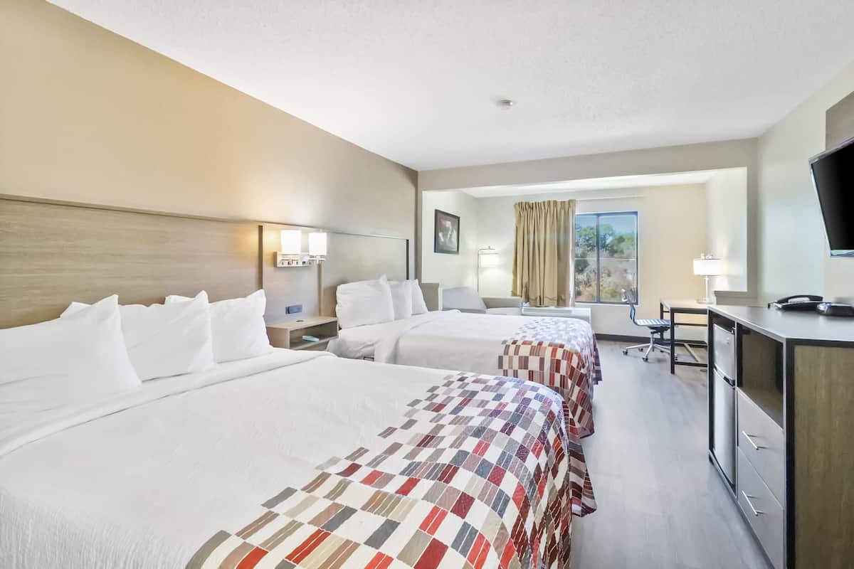 A hotel room with two beds, a desk, a chair, a TV, and a window with curtains.