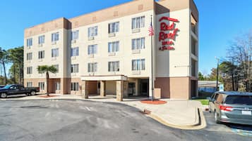 Un hotel de varios pisos con fachada color crema, un letrero rojo que dice "Red Roof Inn", y un estacionamiento con varios vehículos.