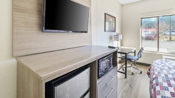 Habitación de hotel con televisor de pantalla plana montado en la pared, un escritorio con una silla y una cama con edredón estampado.