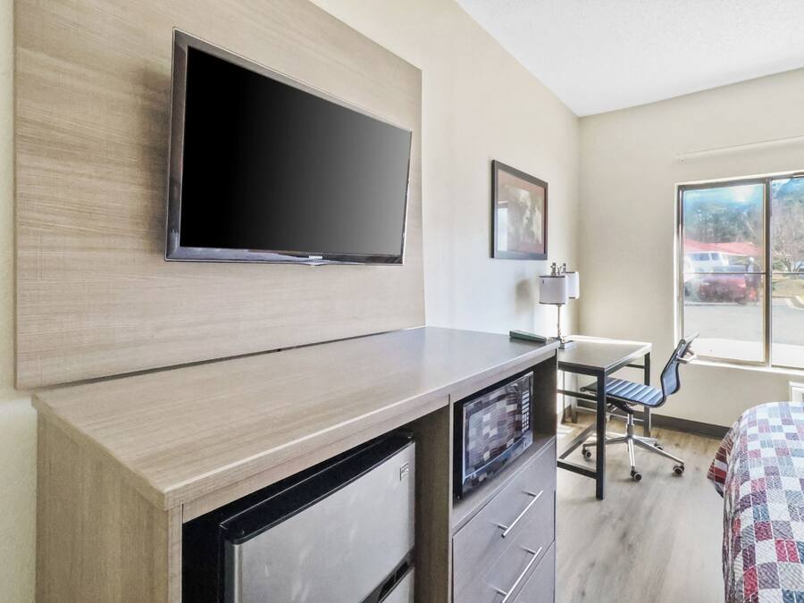 A hotel room with a flat-screen TV mounted on the wall, a desk with a chair, and a bed with a patterned bedspread.