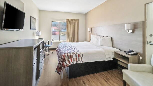 A hotel room with a bed, a desk, a chair, a television, and a window with curtains. - Red Roof Inn & Suites Fayetteville - Fort Bragg (Fayetteville)