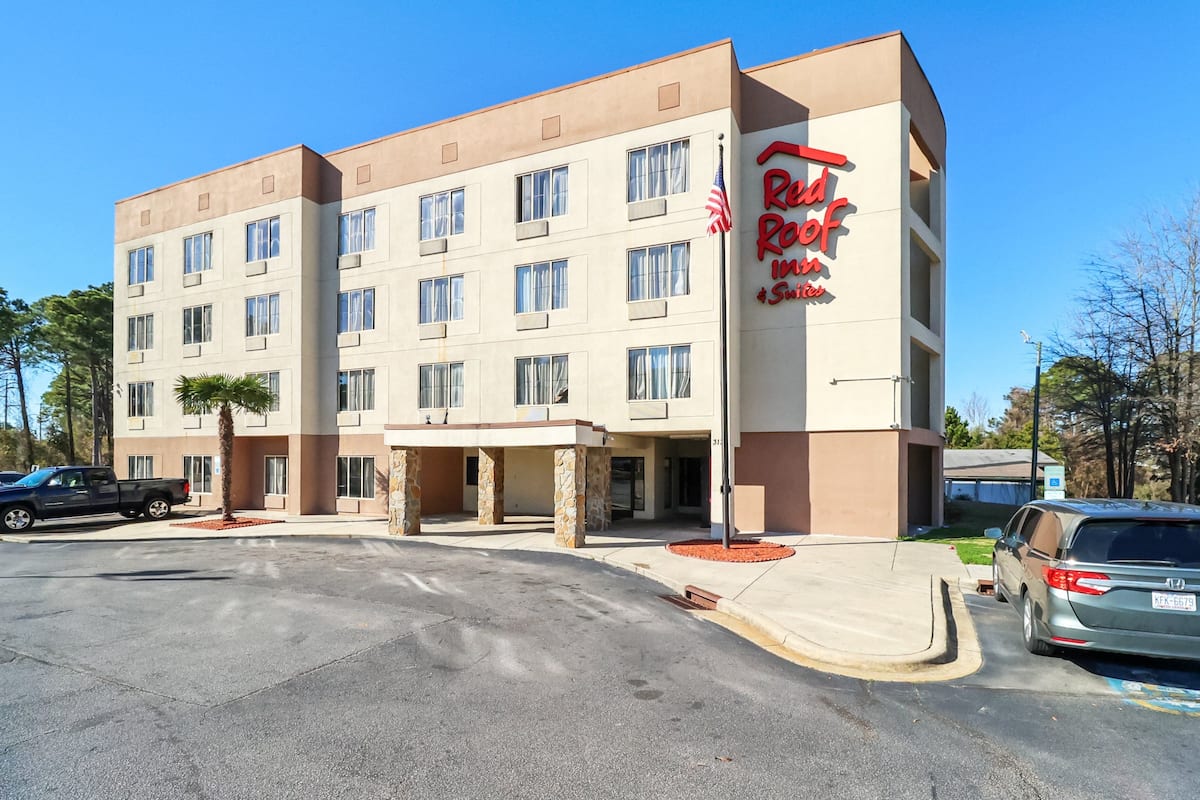 A multi-story hotel with a beige facade, a red sign reading "Red Roof Inn," and a parking lot with several vehicles.