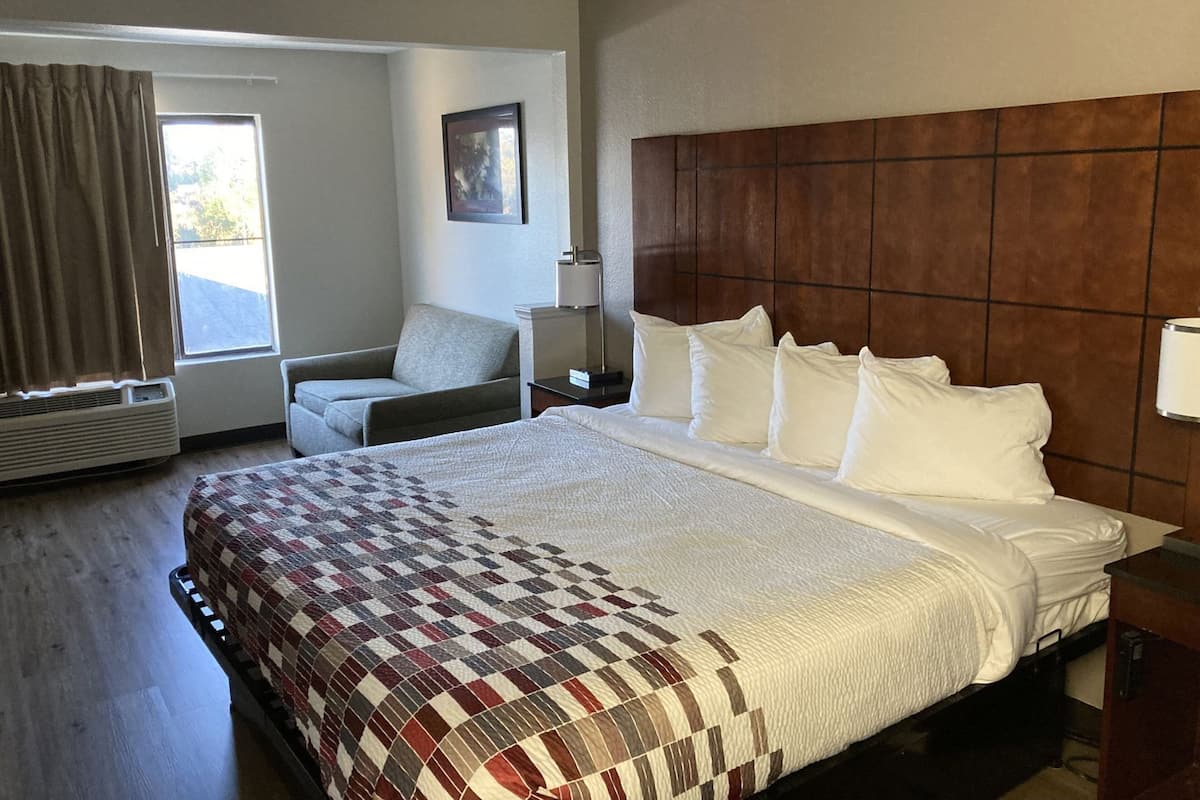 A hotel room with a large bed, a chair, a desk, and a window.