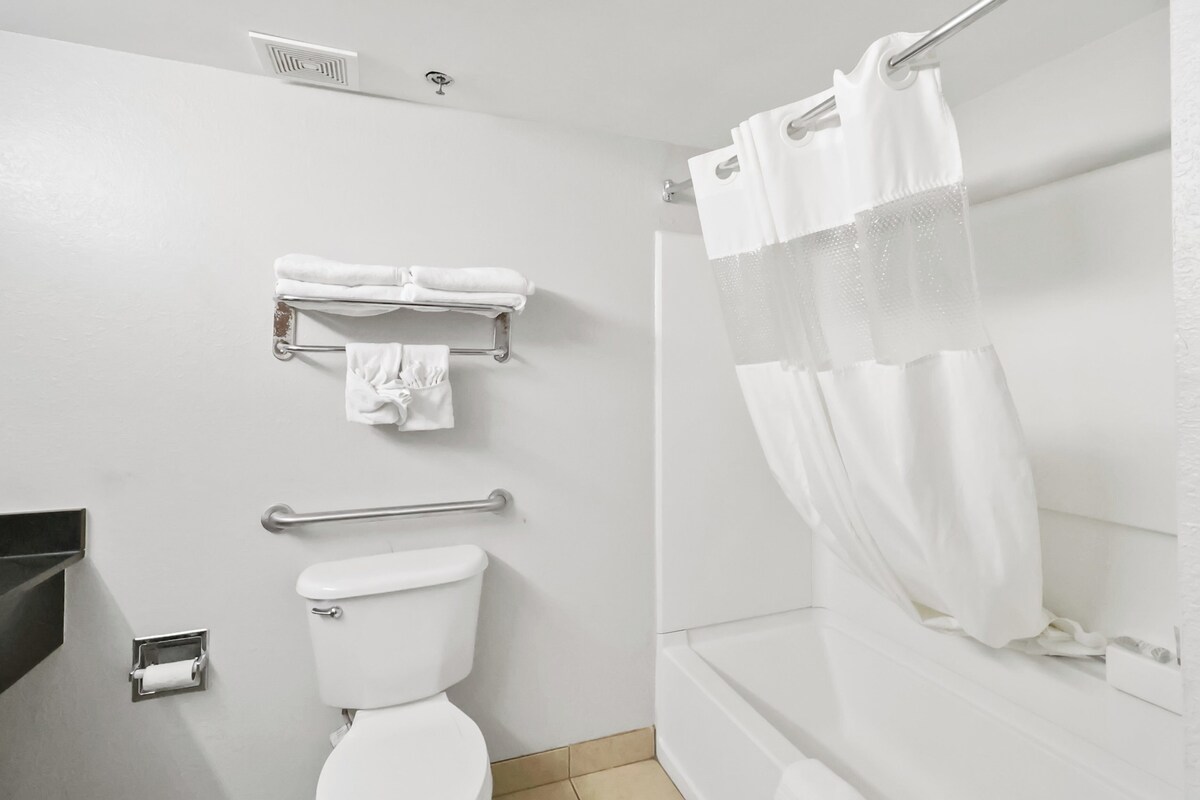 Un baño con inodoro, toallero, cortina de ducha y barandilla.