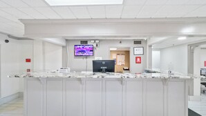 A reception area with a marble counter, a flat-screen TV, a computer, and a fire alarm on the wall. - Red Roof Inn & Suites Fayetteville - Fort Bragg (Fayetteville)