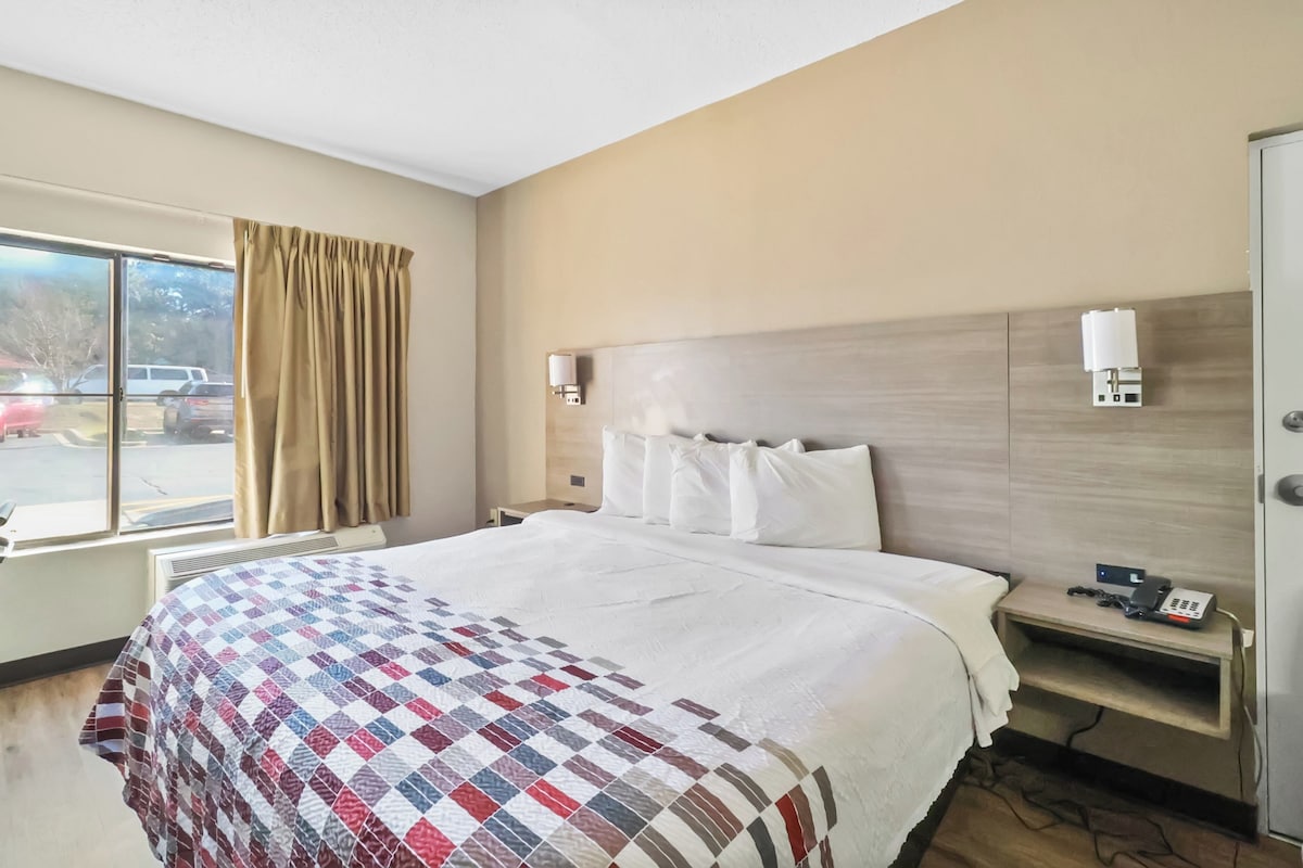 Ein Hotelzimmer mit einem großen Bett, einem Nachttisch mit Telefon und einem Fenster mit Vorhängen.