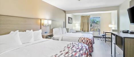 A hotel room with two beds, a desk, a chair, a television, and a window with curtains.