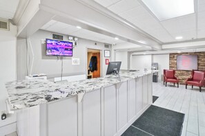 A reception area with a marble counter, a television mounted on the wall, a computer, and two red chairs.