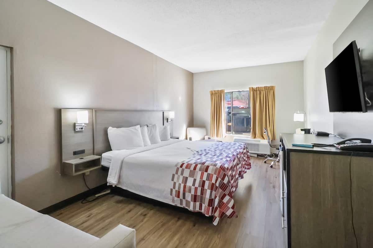 A hotel room with a bed, bedside tables, a desk, a flat-screen TV, and a window with curtains.