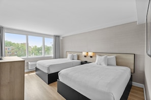 A hotel room with two beds, a desk, and a large window.