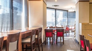 Un restaurant avec des tables et des chaises en bois, de grandes fenêtres et une vue sur la rue.