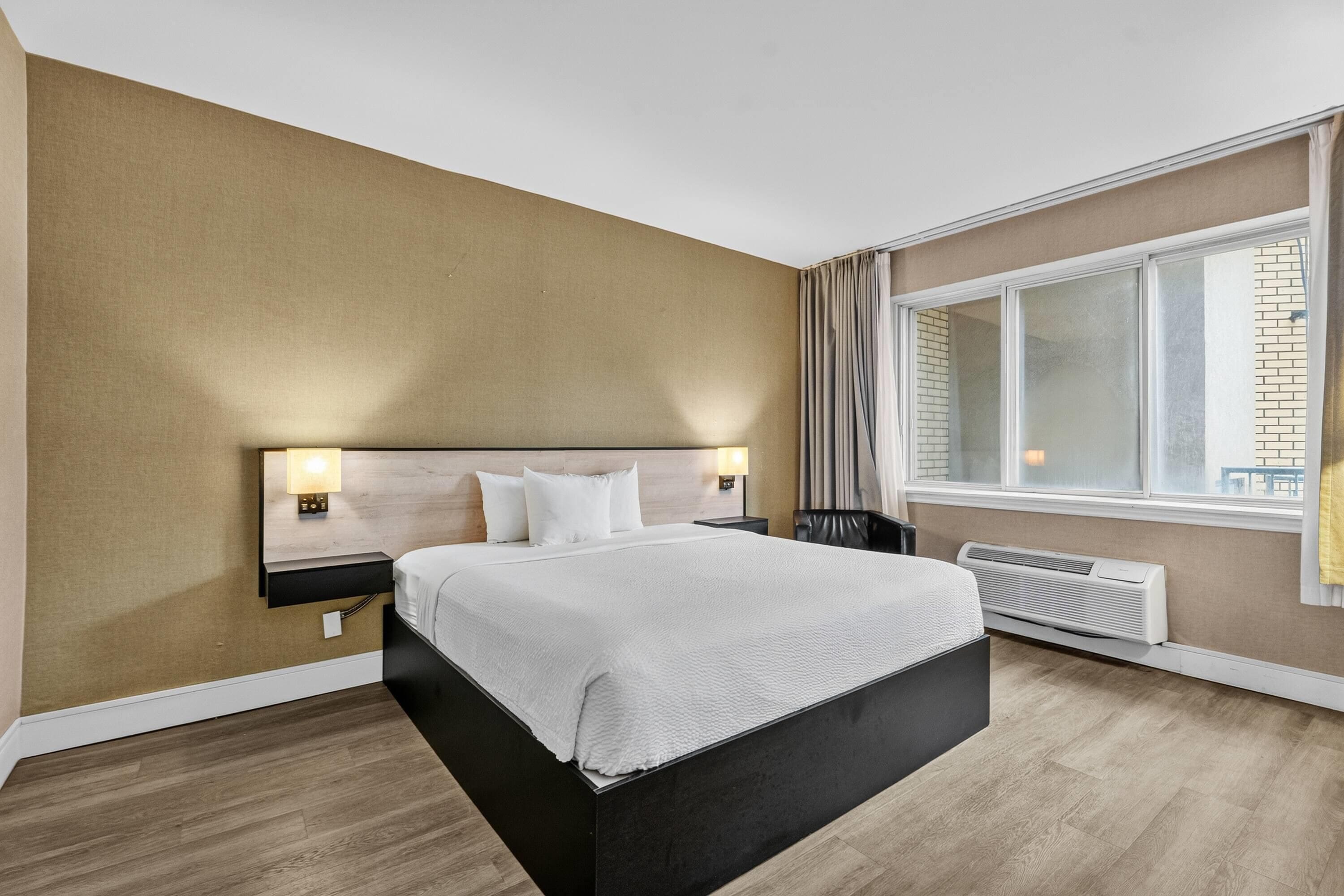 Une chambre d’hôtel avec un lit, des lampes de chevet, une fenêtre avec des rideaux, un radiateur et une vue sur l’extérieur.