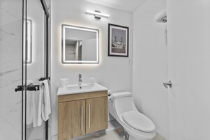 Une salle de bain moderne avec une douche à parois de verre, un meuble-lavabo en bois, des toilettes blanches et un tableau encadré au mur.