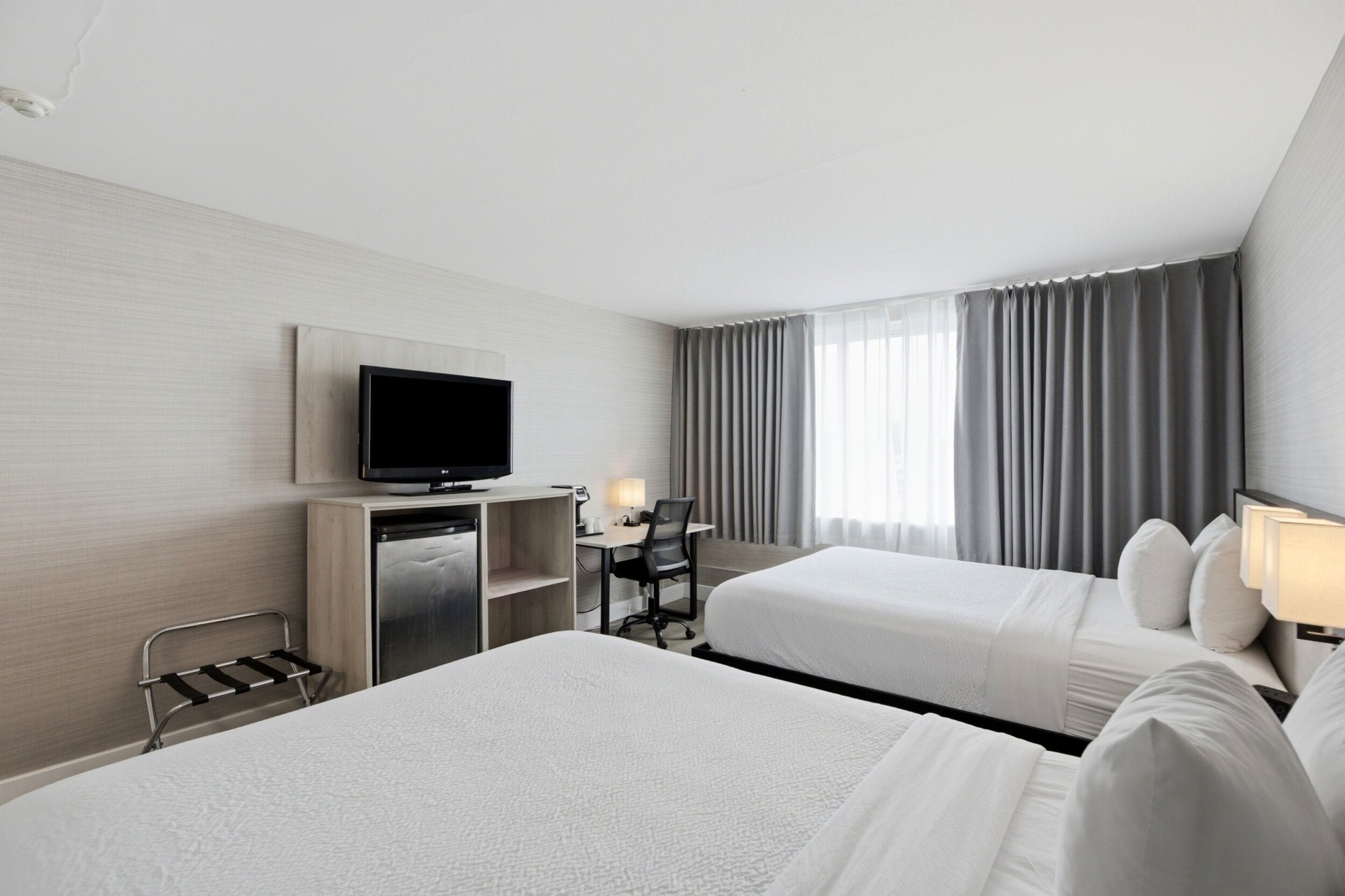 A hotel room with two beds, a desk, a television, and a minibar.