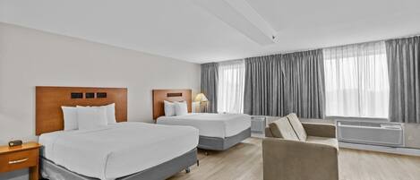 Une chambre d’hôtel avec deux lits, un canapé, une table de chevet et une fenêtre avec des rideaux.