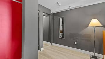 Un pasillo con una pared roja, una pared gris y un suelo de madera. Hay un espejo en la pared gris y una lámpara a la derecha.