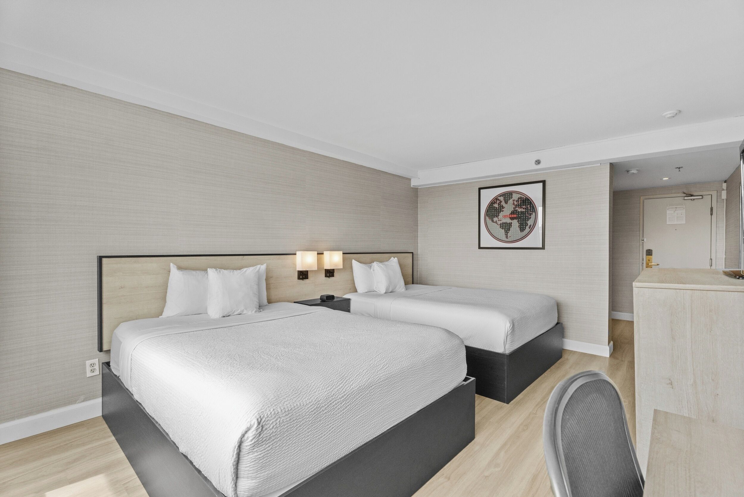 A hotel room with two beds, a desk, and a chair.