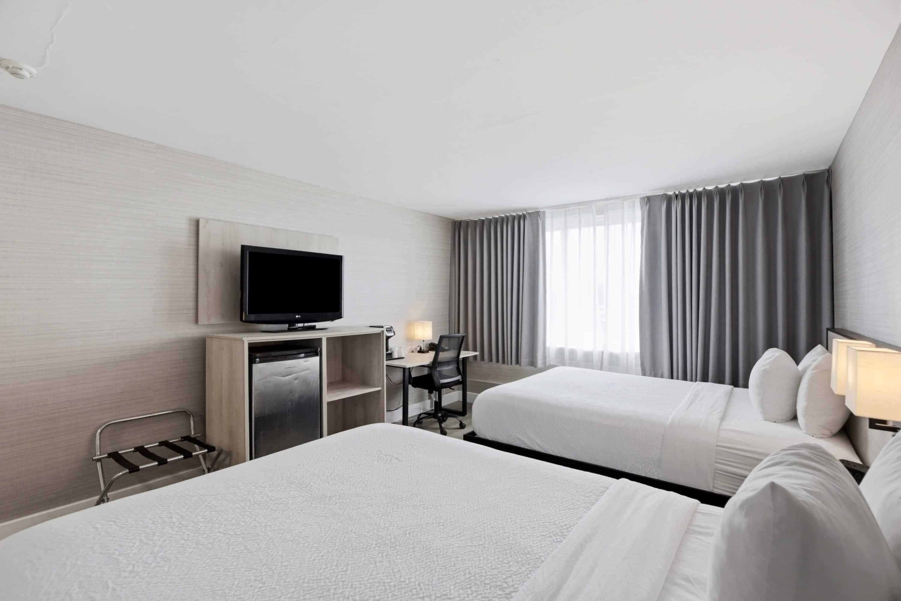 A hotel room with two beds, a desk with a chair, a television, and a window with curtains.