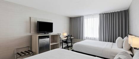 A hotel room with two beds, a desk with a chair, a television, and a window with curtains.