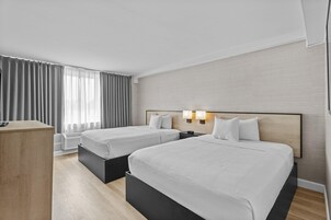 Une chambre d’hôtel avec deux lits, un bureau et une fenêtre avec des rideaux.