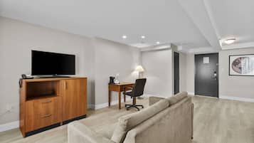 Una sala moderna con una televisión de pantalla plana sobre un mueble de madera, un sofá color beige, un escritorio con una lámpara y una puerta con una obra de arte circular.