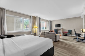 Habitación de hotel con cama, escritorio, silla, televisión y ventana con cortinas.