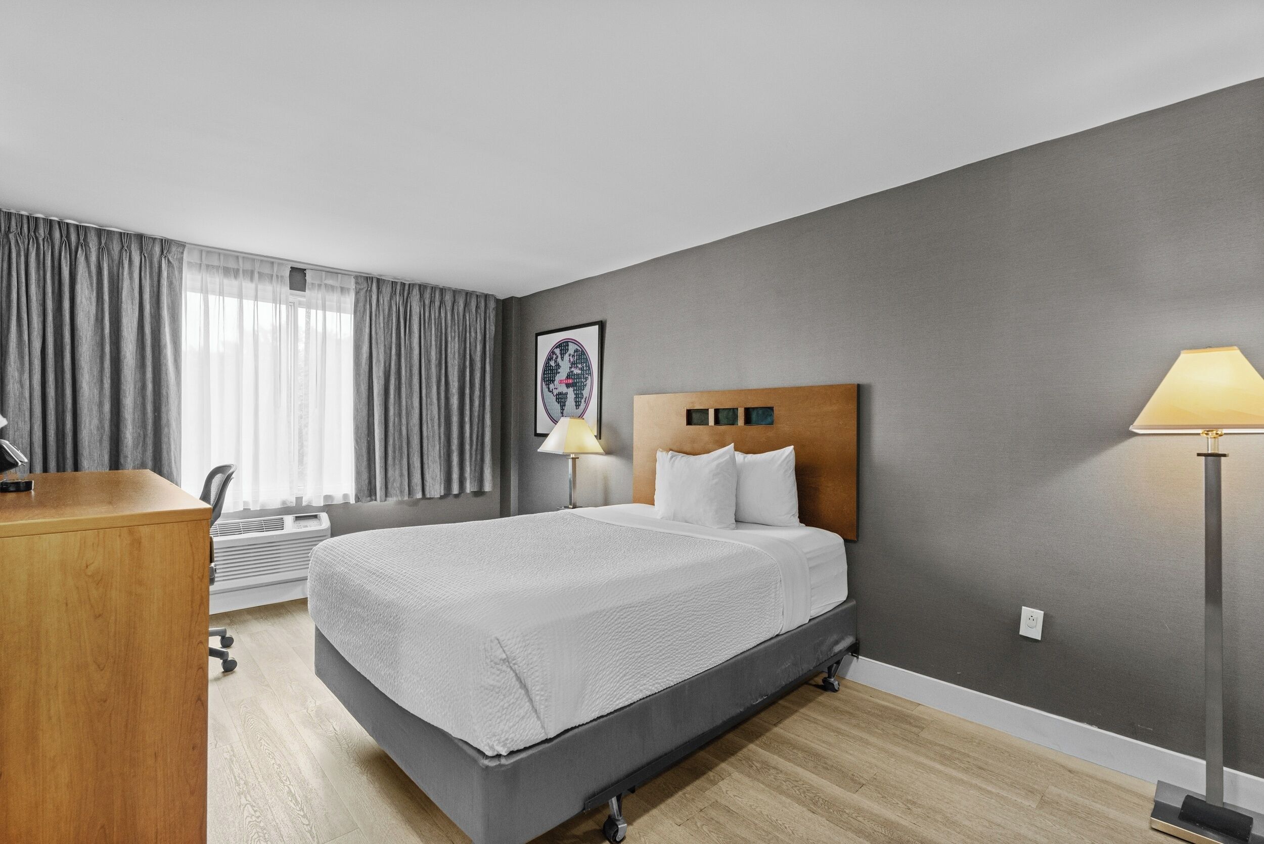 Une chambre d’hôtel avec un lit, un bureau, une chaise, une lampe et un tableau au mur.