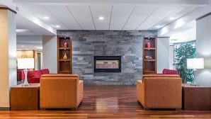 Un vestíbulo con dos sofás orientados hacia una pared de piedra con un televisor. Se observan mesitas de madera con lámparas, y una planta al fondo.