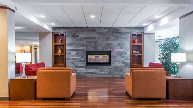 Un vestíbulo con dos sofás orientados hacia una pared de piedra con un televisor. Se observan mesitas de madera con lámparas, y una planta al fondo.