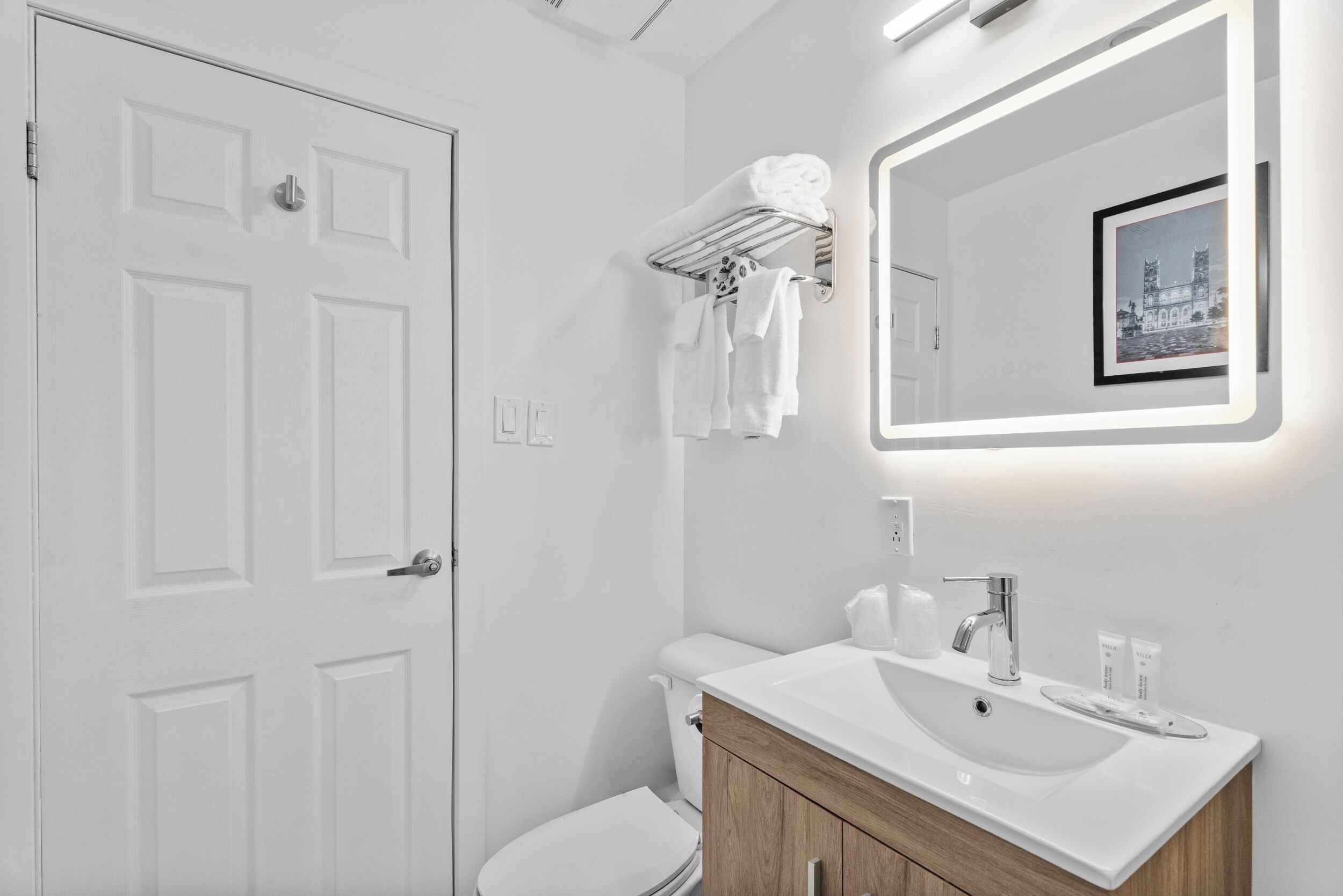 A modern bathroom with a white door, a toilet, a vanity with a sink, and a towel rack.