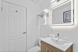 Egy modern fürőszoba, fehér ajtóval, WC-vel, mosdókagylós fürdőszobai mosdóval és törölközőtartóval.