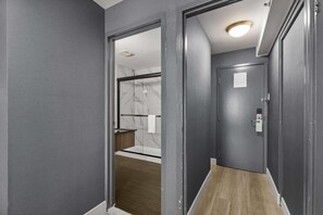 Un couloir avec une porte donnant sur une salle de bain équipée d’une douche en marbre et d’un plancher en bois.