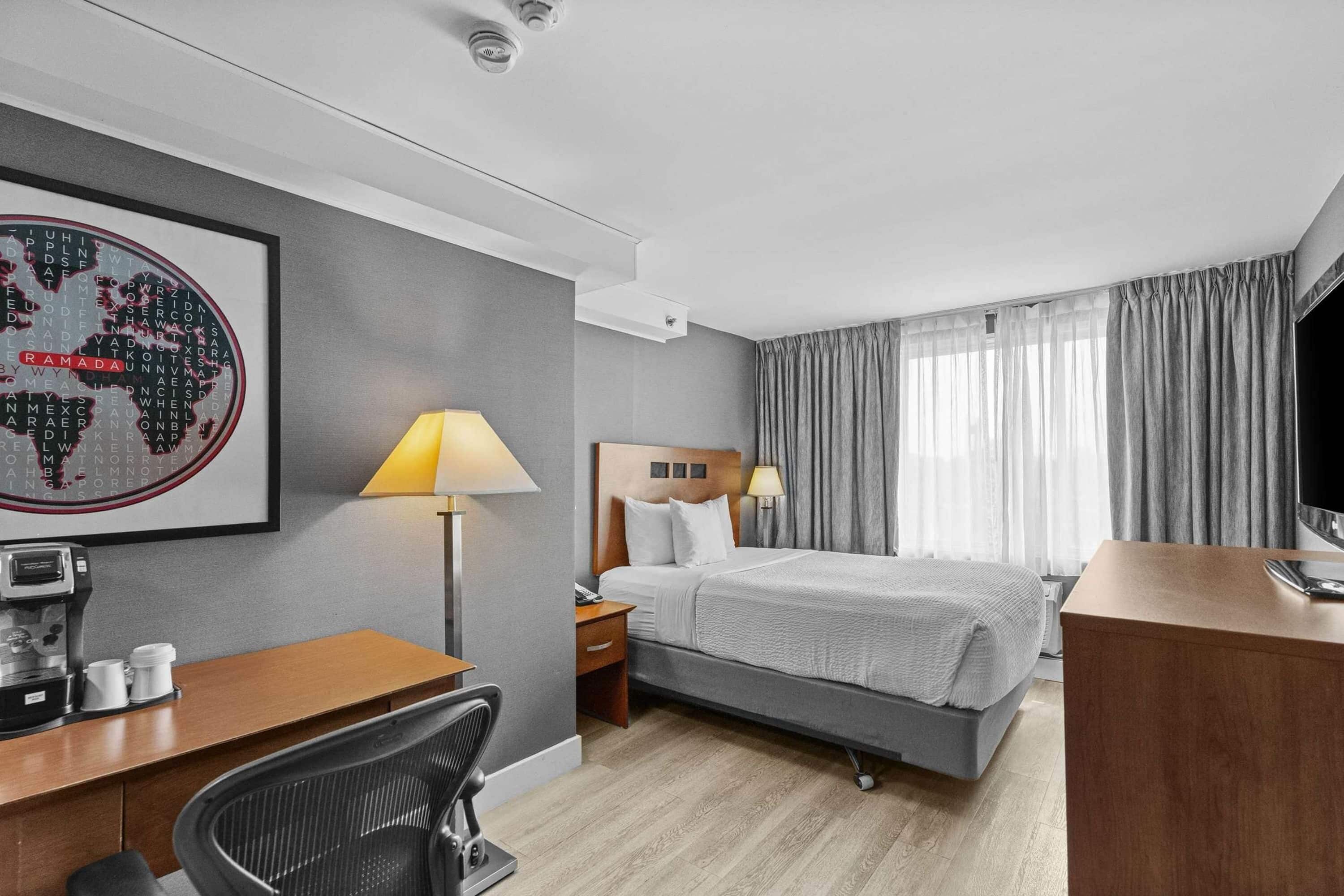A hotel room with a bed, a desk with a coffee maker, a chair, a lamp, and a world map on the wall.