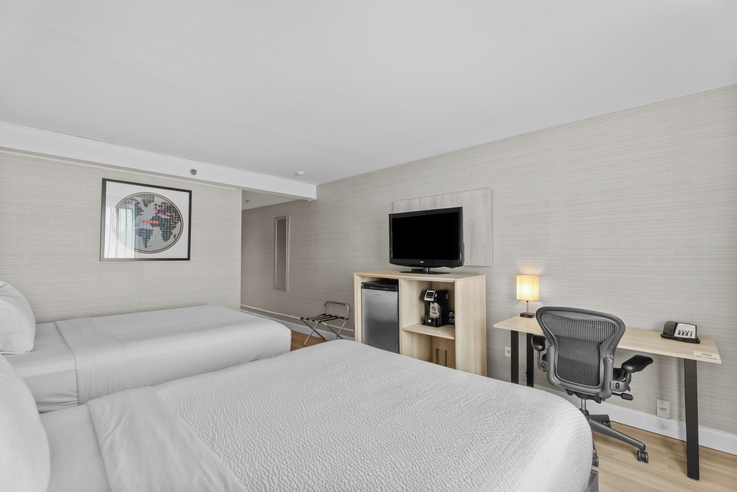 A hotel room with a bed, a desk with a computer, a television, and a coffee machine.