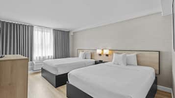 A hotel room with two beds, a desk, and a window with curtains.