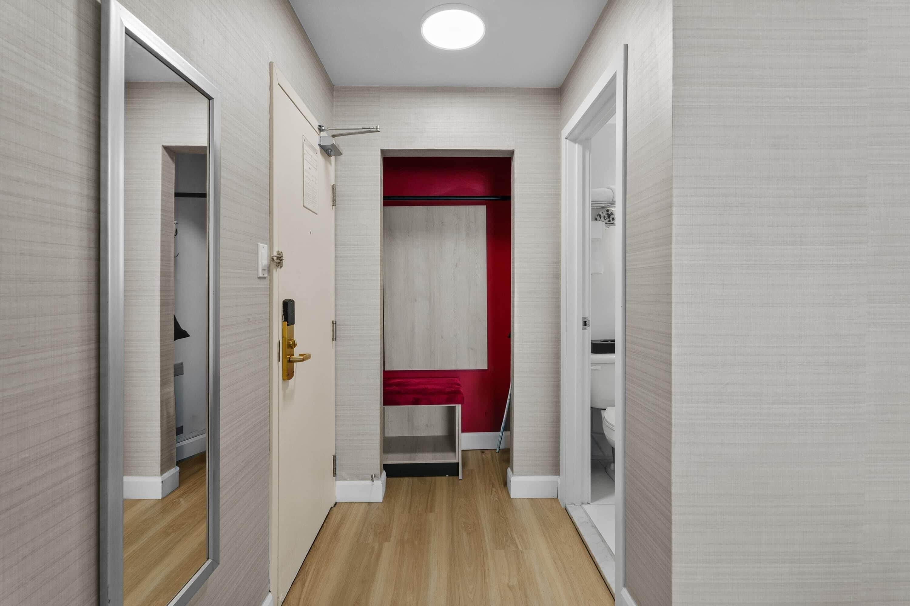 Un pasillo con suelo de madera, una pared de acento roja y una puerta blanca con pomo dorado.