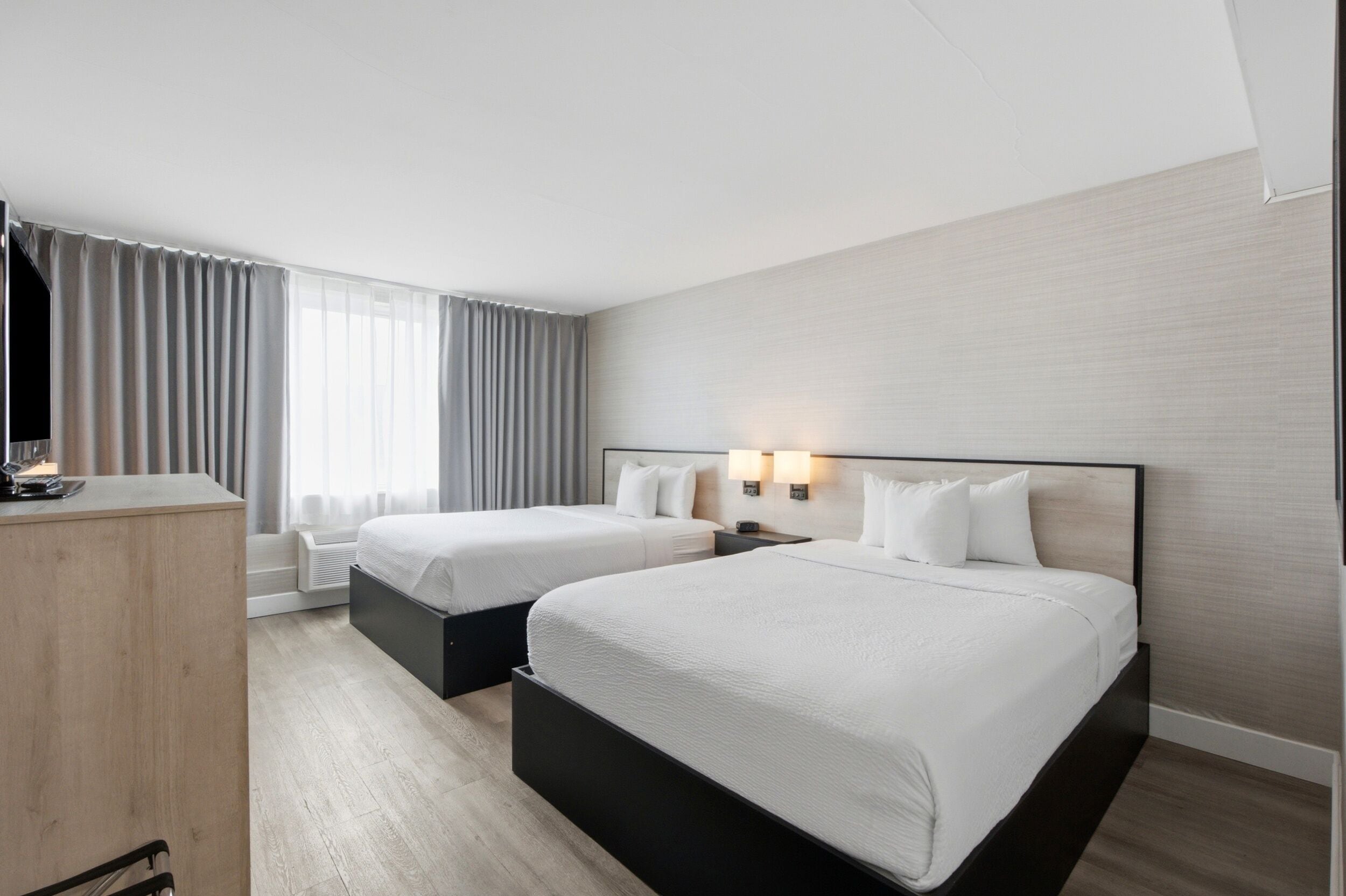 A hotel room with two beds, a desk, and a large window with curtains.